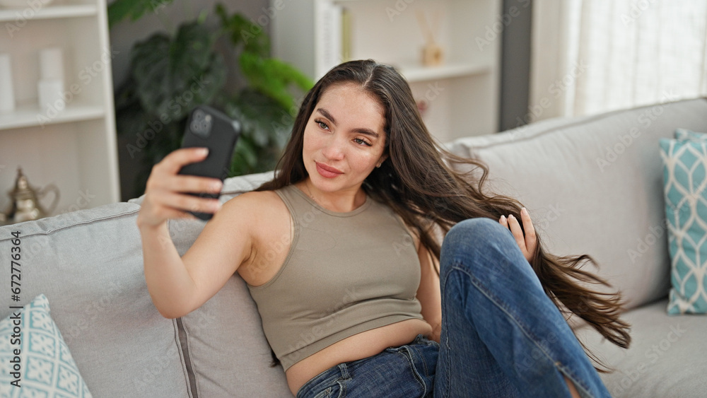 Obraz premium Young beautiful hispanic woman taking selfie picture with smartphone sitting on the sofa at home