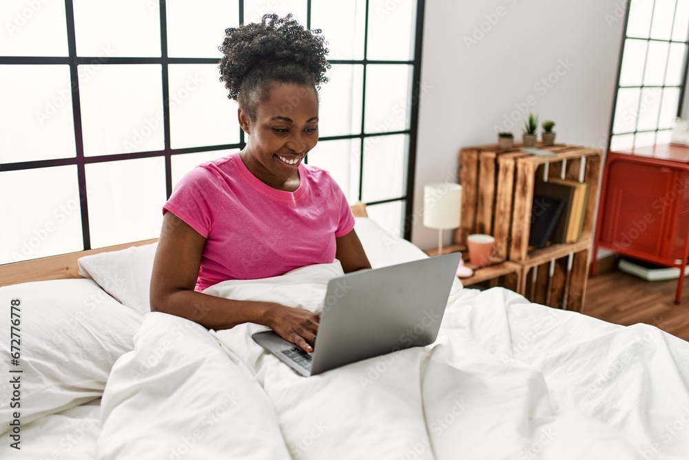 African american woman using laptop sitting on bed at bedroom African american woman using laptop sitting on bed at bedroom