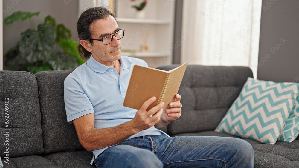 Middle age man reading book sitting on sofa at home