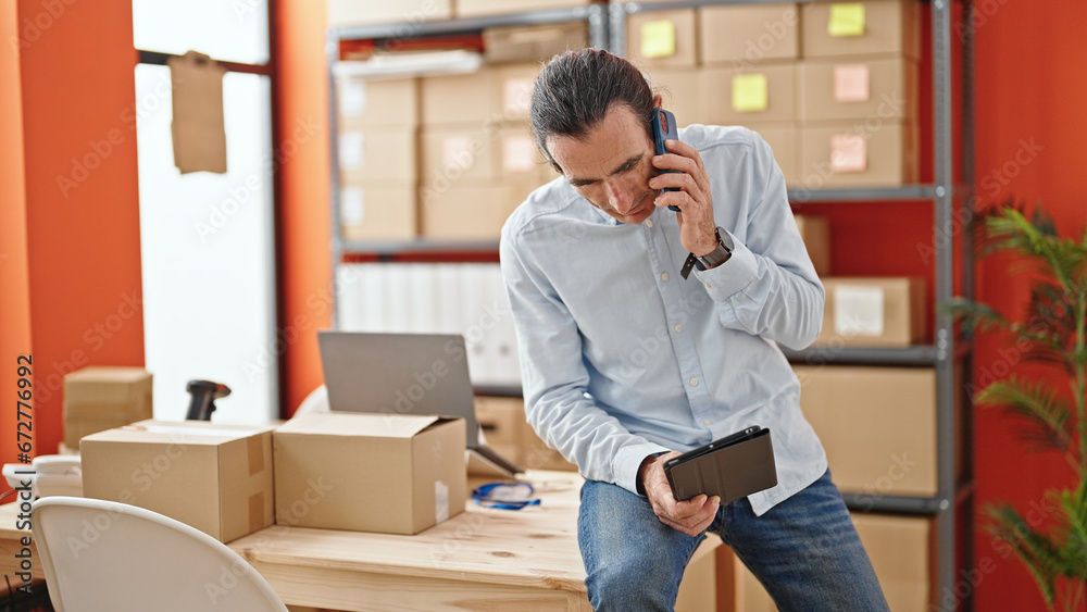Middle age man ecommerce business worker using touchpad talking on smartphone at office Middle age man ecommerce business worker using touchpad talking on smartphone at office