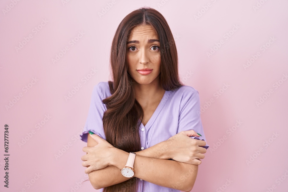 Young hispanic woman with long hair standing over pink background shaking and freezing for winter cold with sad and shock expression on face Young hispanic woman with long hair standing over pink background shaking and freezing for winter cold with sad and shock expression on face