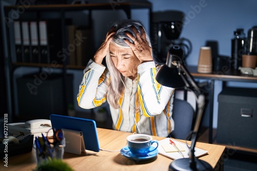 Obraz na plátně Middle age woman with grey hair working at the office at night suffering from headache desperate and stressed because pain and migraine