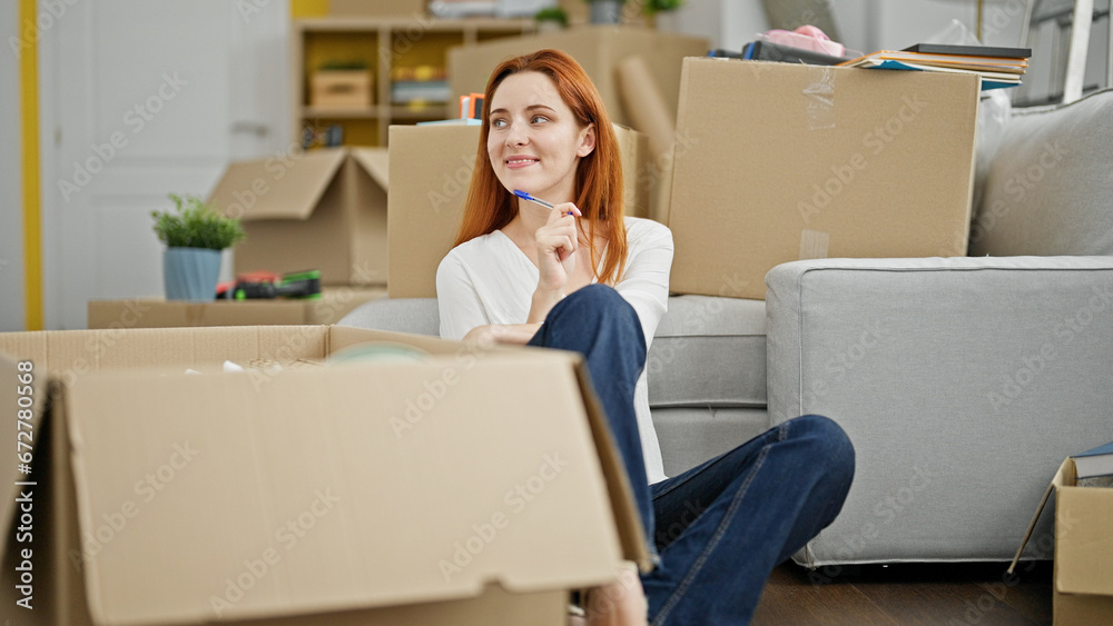 Young redhead woman sitting on floor thinking at new home Young redhead woman sitting on floor thinking at new home