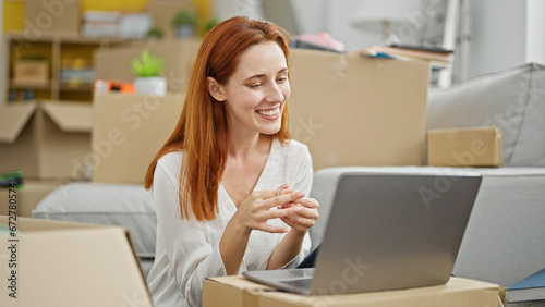 Young redhead woman using laptop sitting on floor at new home