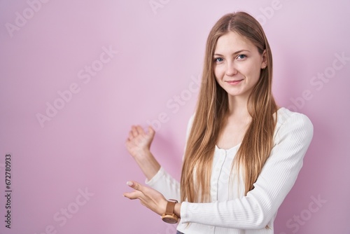 Young caucasian woman standing over pink background inviting to enter smiling natural with open hand
