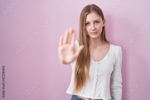 Young caucasian woman standing over pink background doing stop sing with palm of the hand. warning expression with negative and serious gesture on the face. © Krakenimages.com