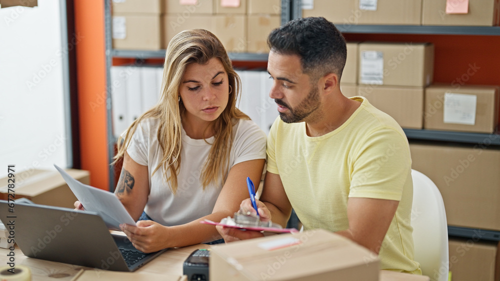 Man and woman ecommerce business workers reading document writing on clipboard at office Man and woman ecommerce business workers reading document writing on clipboard at office