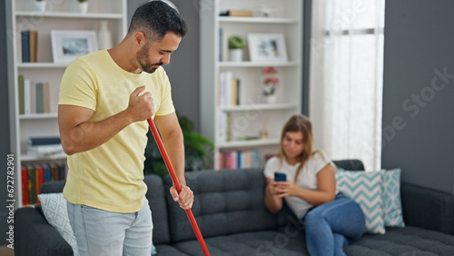 Man and woman couple doing chores while girlfriend use smartphone at home