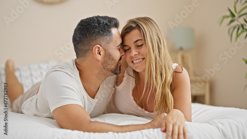 Man and woman couple lying on bed hugging each other kissing at bedroom