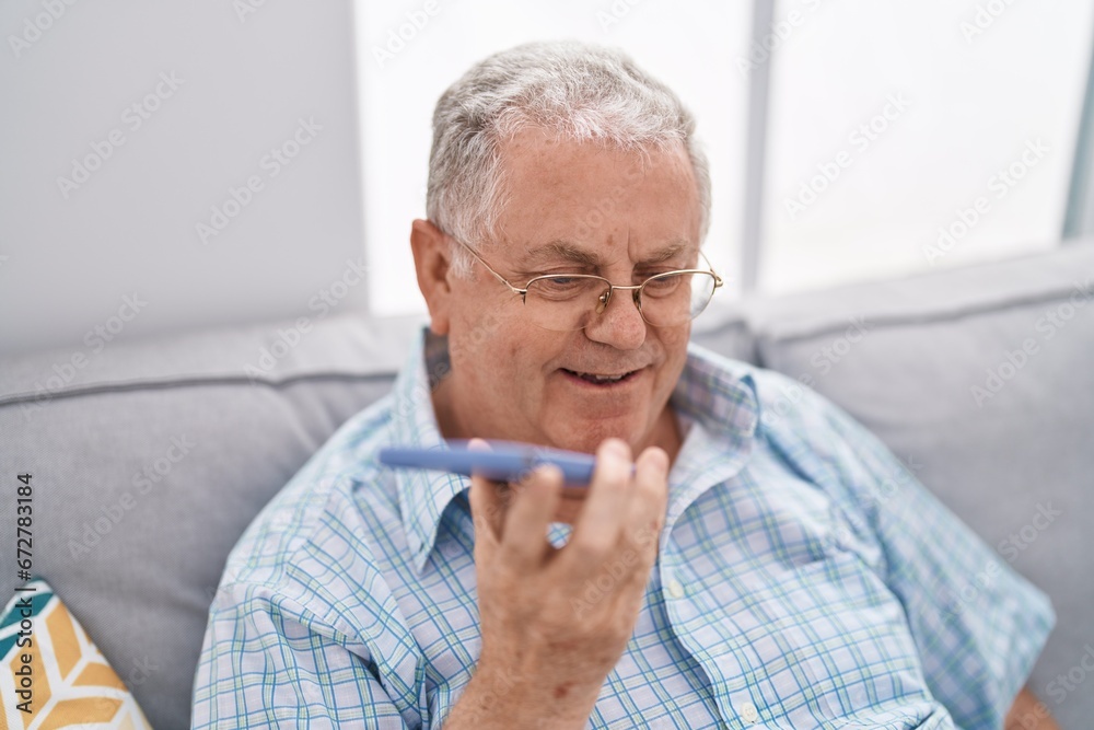 Middle age grey-haired man talking on the smartphone sitting on sofa at home