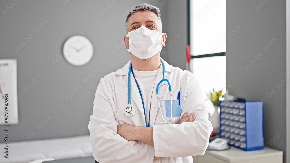 Young caucasian man doctor standing with arms crossed gesture wearing medical mask at the clinic Young caucasian man doctor standing with arms crossed gesture wearing medical mask at the clinic