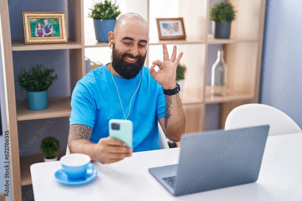 Young hispanic man with beard and tattoos doing video call with smartphone doing ok sign with fingers, smiling friendly gesturing excellent symbol Young hispanic man with beard and tattoos doing video call with smartphone doing ok sign with fingers, smiling friendly gesturing excellent symbol