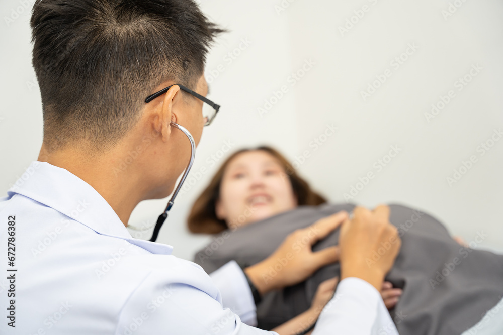 Fototapeta premium Male doctor is checking pregnant woman with stethoscope at hospital. Concept caring for pregnant woman