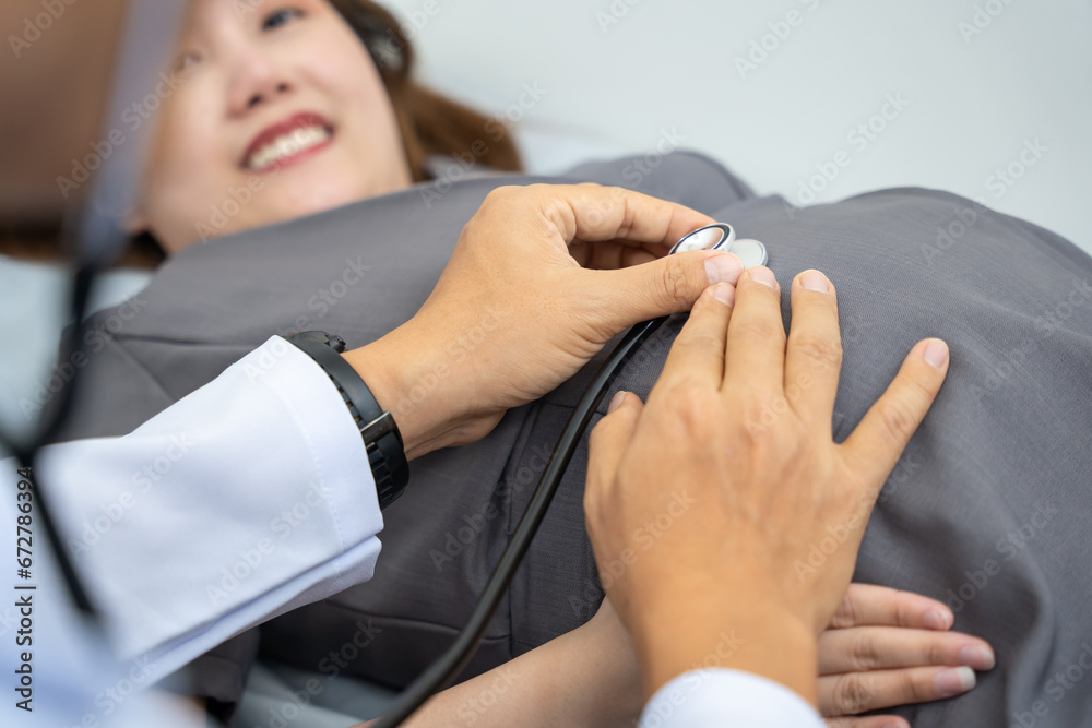 Fototapeta premium Male doctor is checking pregnant woman with stethoscope at hospital. Concept caring for pregnant woman