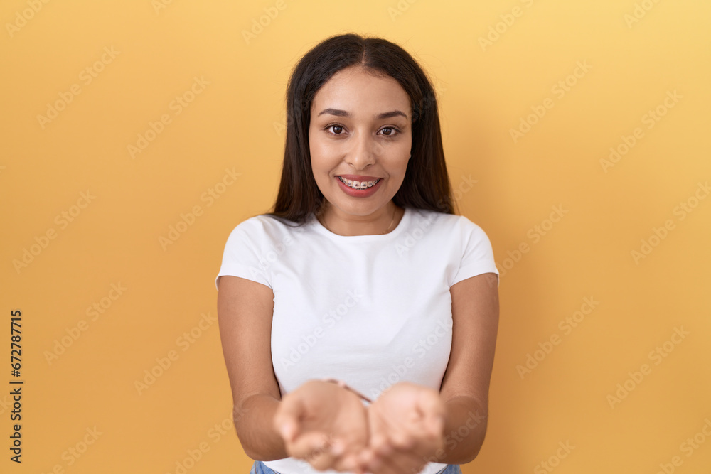 Obraz premium Young arab woman wearing casual white t shirt over yellow background smiling with hands palms together receiving or giving gesture. hold and protection