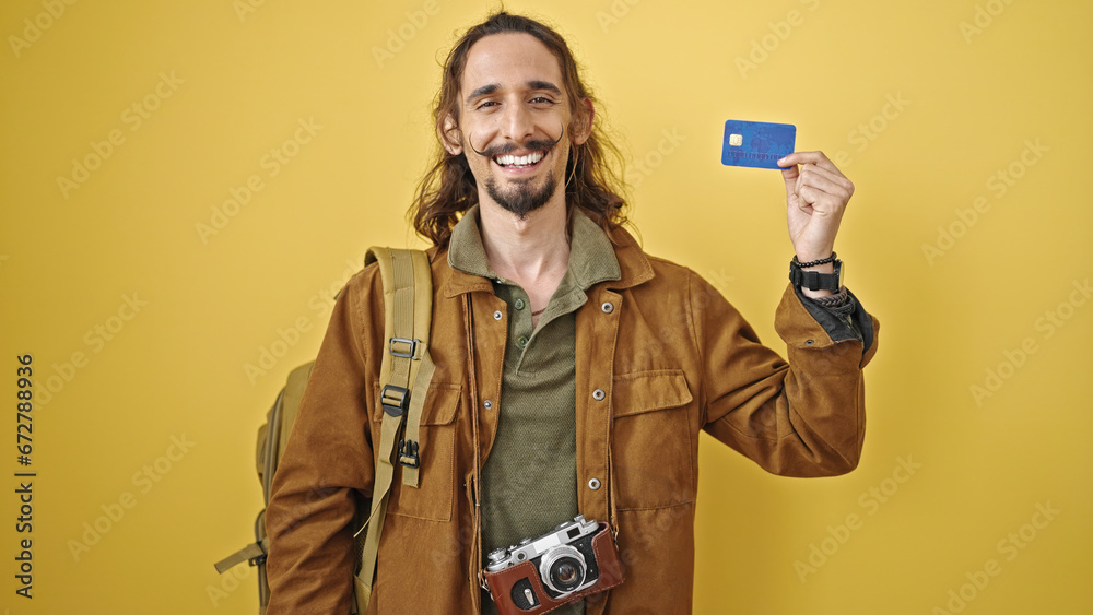 Young hispanic man tourist holding credit card smiling over isolated yellow background Young hispanic man tourist holding credit card smiling over isolated yellow background