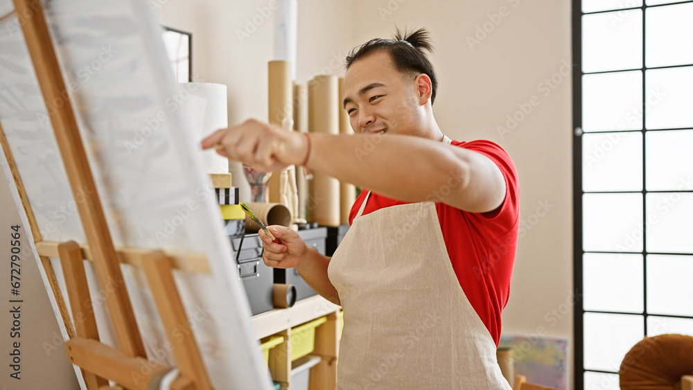 Confident young chinese artist smiling as he enjoys drawing in a vibrant art studio, embodying creativity with a brush and canvas Confident young chinese artist smiling as he enjoys drawing in a vibrant art studio, embodying creativity with a brush and canvas