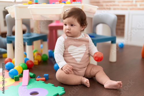 Adorable toddler holding plastic ball sitting on floor at kindergarten