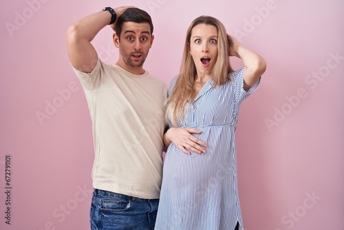 Young couple expecting a baby standing over pink background crazy and scared with hands on head, afraid and surprised of shock with open mouth © Krakenimages.com