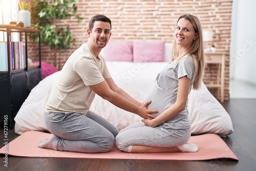 Man and woman couple expecting belly doing prepartum exercise at bedroom