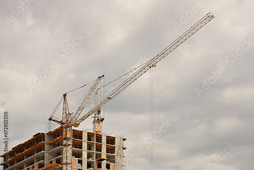 Tower cranes work during the construction of a multi-story building. New apartments for residents and premises for offices. Risky work at height. Lifting heavy building materials. City development © Xato Lux