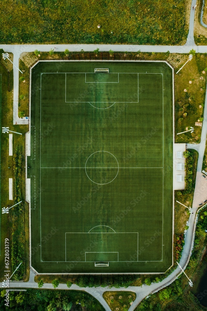 Aerial shot of a lush green soccer field in a rural area, surrounded by tall trees
