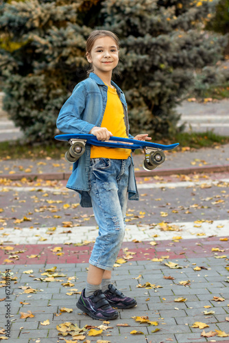 A young girl holds a skateboard in an autumn park.