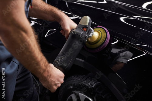 Canvas Print Professional auto detailer hand holding rotary polisher while polishing paint surface of shiny black car