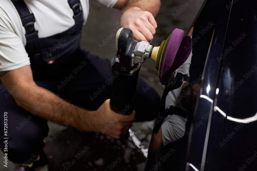 Cropped auto detailer hand holding rotary polisher while polishing paint surface of shiny black car. Car detailing, car wash, and paint correction concept. Cropped photo. Selective focus. Cropped auto detailer hand holding rotary polisher while polishing paint surface of shiny black car. Car detailing, car wash, and paint correction concept. Cropped photo. Selective focus.