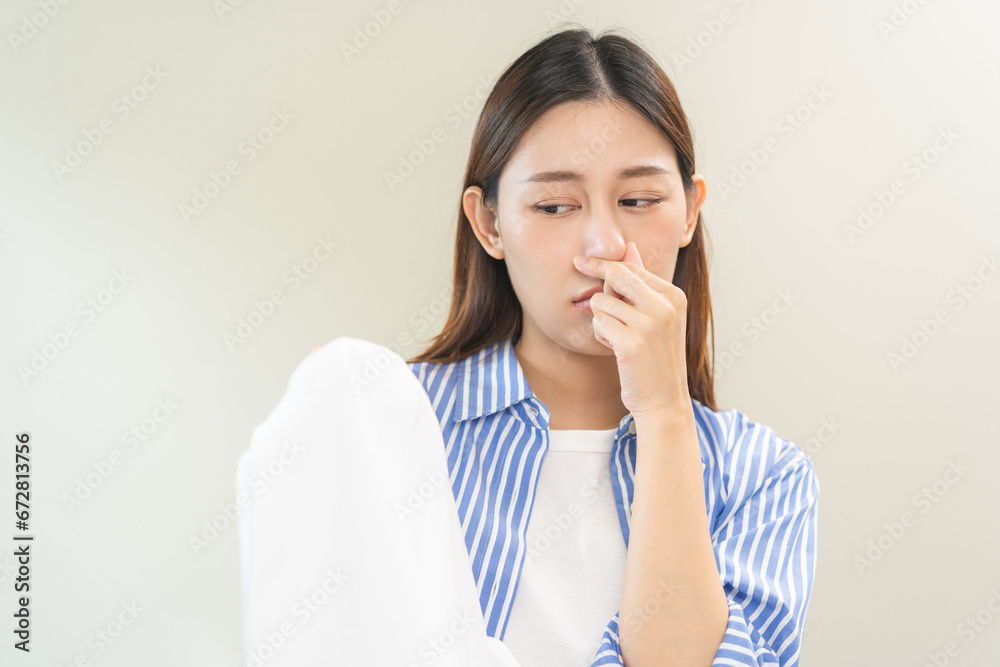 Asian young housewife woman having bad smelling clothes hand holding breath nose with finger, sniff smelly dirty stinky musty, look disgusting from clothes after washed, laundry out of machine at home Asian young housewife woman having bad smelling clothes hand holding breath nose with finger, sniff smelly dirty stinky musty, look disgusting from clothes after washed, laundry out of machine at home