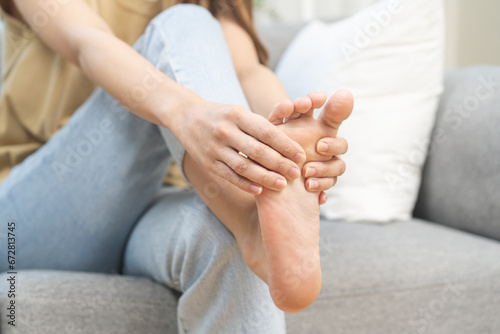 Foot pain concept, close up hand of young woman rubbing, massaging sore feet area of pain, girl suffering on sofa, couch at home. Discomfort painful feet ache from walking for long. Physical injury. © KMPZZZ