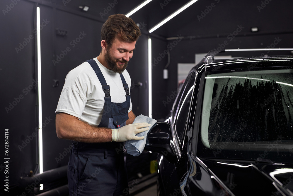 Man cleaning car and drying vehicle with microfiber cloth. male wipe down paint surface of shiny black car after polishing and ceramic coating. Car detailing and car wash concept