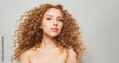 Young woman with wavy hair and natural makeup. Fashion model with long curly hairstyle and fresh clear skin posing on white background