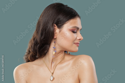 Beautiful lady portrait. Brunette woman in gold jewelry earring with amethyst and opal posing on blue background