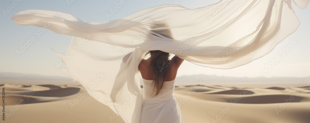 Woman in a long white dress walking in the desert with flowing fabric in the wind Woman in a long white dress walking in the desert with flowing fabric in the wind