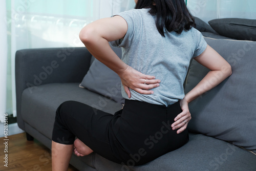 Asian woman aching back spinal pain from stress of injury, painful ache stress muscle cramp, body upper muscle problem, indeed of medical physical therapy concept, home living room coach lifestyle photo