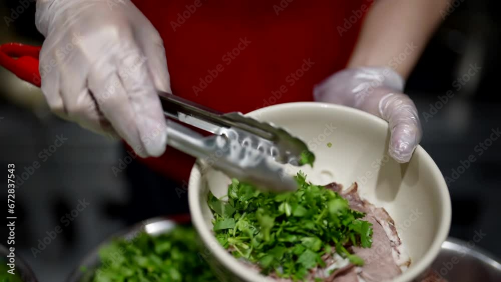 Vietnamese cook making traditional soup Pho with meat and greenery, putting ingredients in bowl Vietnamese cook making traditional soup Pho with meat and greenery, putting ingredients in bowl