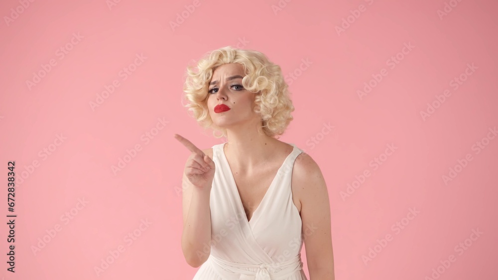The woman points her index finger to the side. Woman in the image of in the studio on a pink background. Advertising, promo, copy space.