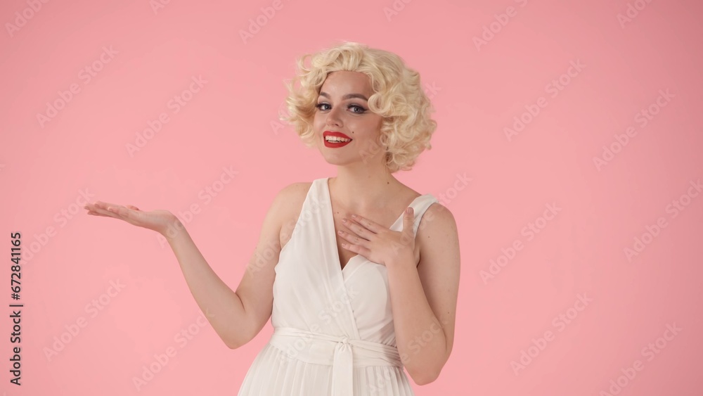 The woman points her hand to the side, recommending. Woman in the image of in the studio on a pink background. Advertising, promo, copy space. The woman points her hand to the side, recommending. Woman in the image of in the studio on a pink background. Advertising, promo, copy space.