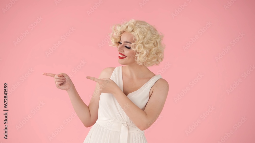 A woman points with her index fingers to something to the side. Woman in the image of in the studio on a pink background. Advertising, promo, copy space. A woman points with her index fingers to something to the side. Woman in the image of in the studio on a pink background. Advertising, promo, copy space.