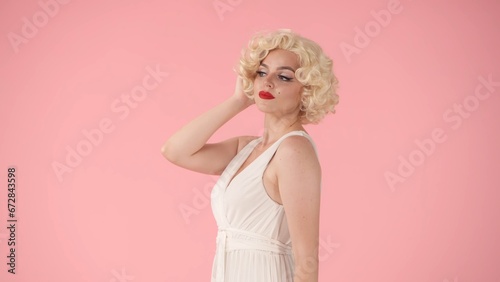Portrait young woman in wig, white dress and with red lipstick on lips in studio on pink background. Woman looking like in studio on pink background. photo