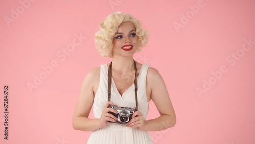 A woman holds up an old vintage camera. Woman in the image of in studio on pink background close up.