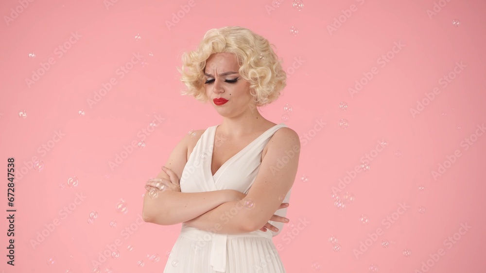 Portrait of a disgruntled woman in the image of surrounded by soap bubbles in studio on pink background. Offended woman standing with her arms crossed on her chest. Portrait of a disgruntled woman in the image of surrounded by soap bubbles in studio on pink background. Offended woman standing with her arms crossed on her chest.