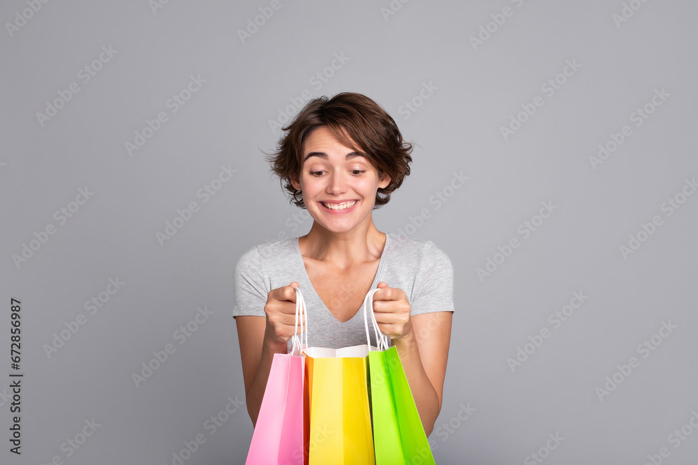 Beautiful excited woman with short hair in t-shirt looking inside colorful shopping bags. Shopping, black Friday, consumer, buyer, sale, store, payment, online buying, discount, purchase, mall