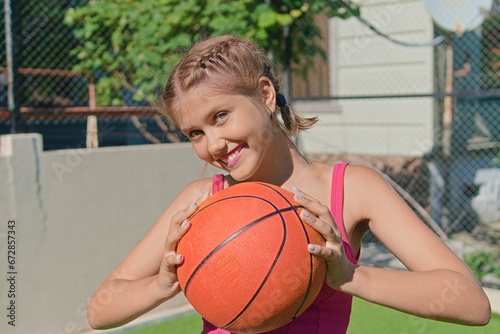 Close-up portrait of a laughing teenage girl holding a basketball on a sports field