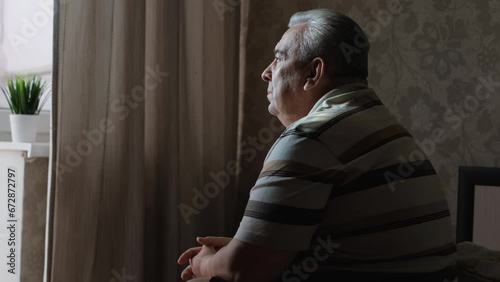 Sad fat elderly man sitting on bed at home