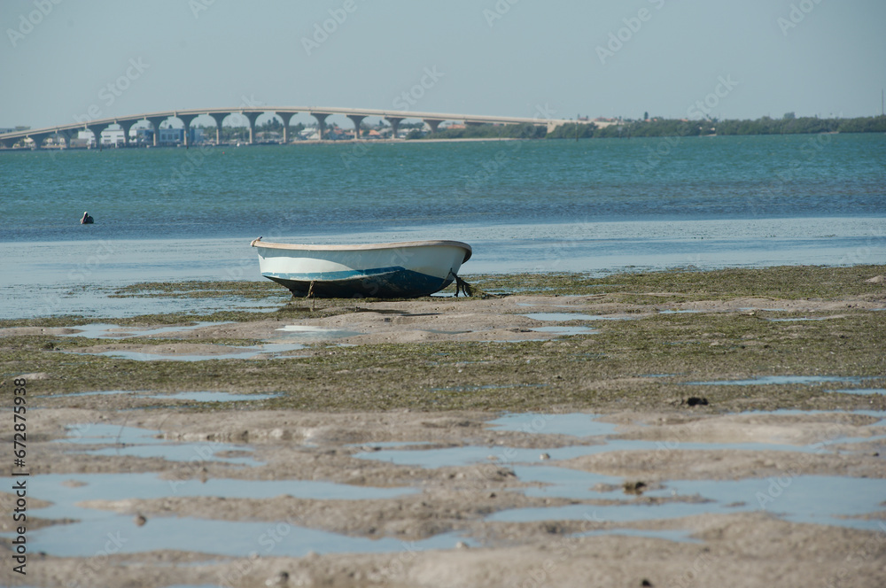 Maximo Beach Park in St. Petersburg, FL. Low tide Small boat isolated on the beach with tide pools in front of the boat from the southern side. Sunny with Tampa Bay and bridge in background. Maximo Beach Park in St. Petersburg, FL. Low tide Small boat isolated on the beach with tide pools in front of the boat from the southern side. Sunny with Tampa Bay and bridge in background.