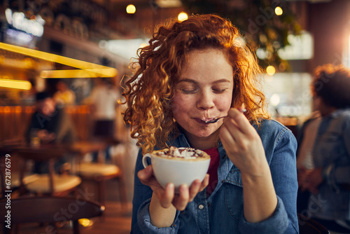 Young woman tasting coffee with spoon in cafe photo