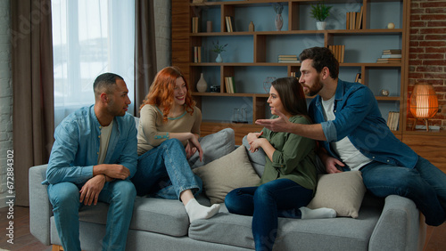 Ethnic friends sit on couch in living room diverse colleagues teammates women girls and men guys smiling talk discuss share plans friendly discussion dialogue laugh friendship weekend meeting at home