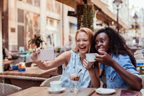 Two happy girlfriends holding smartphone in outdoor cafe photo